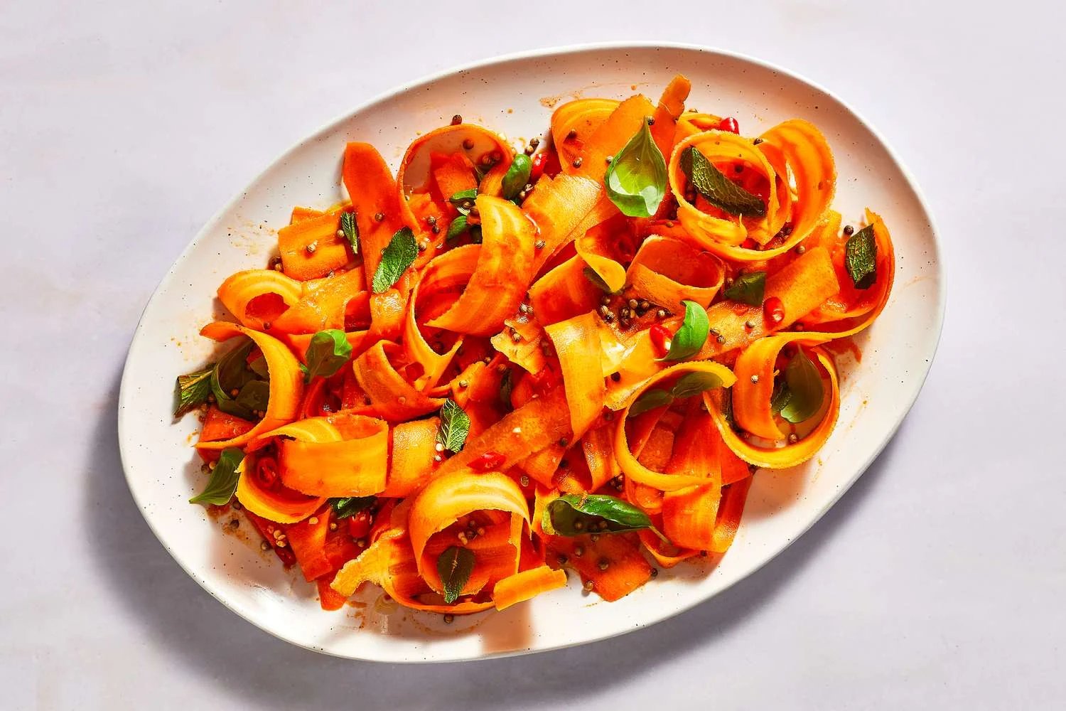 A platter with carrot ribbon salad, garnished with mint, basil, and birds eye chilies