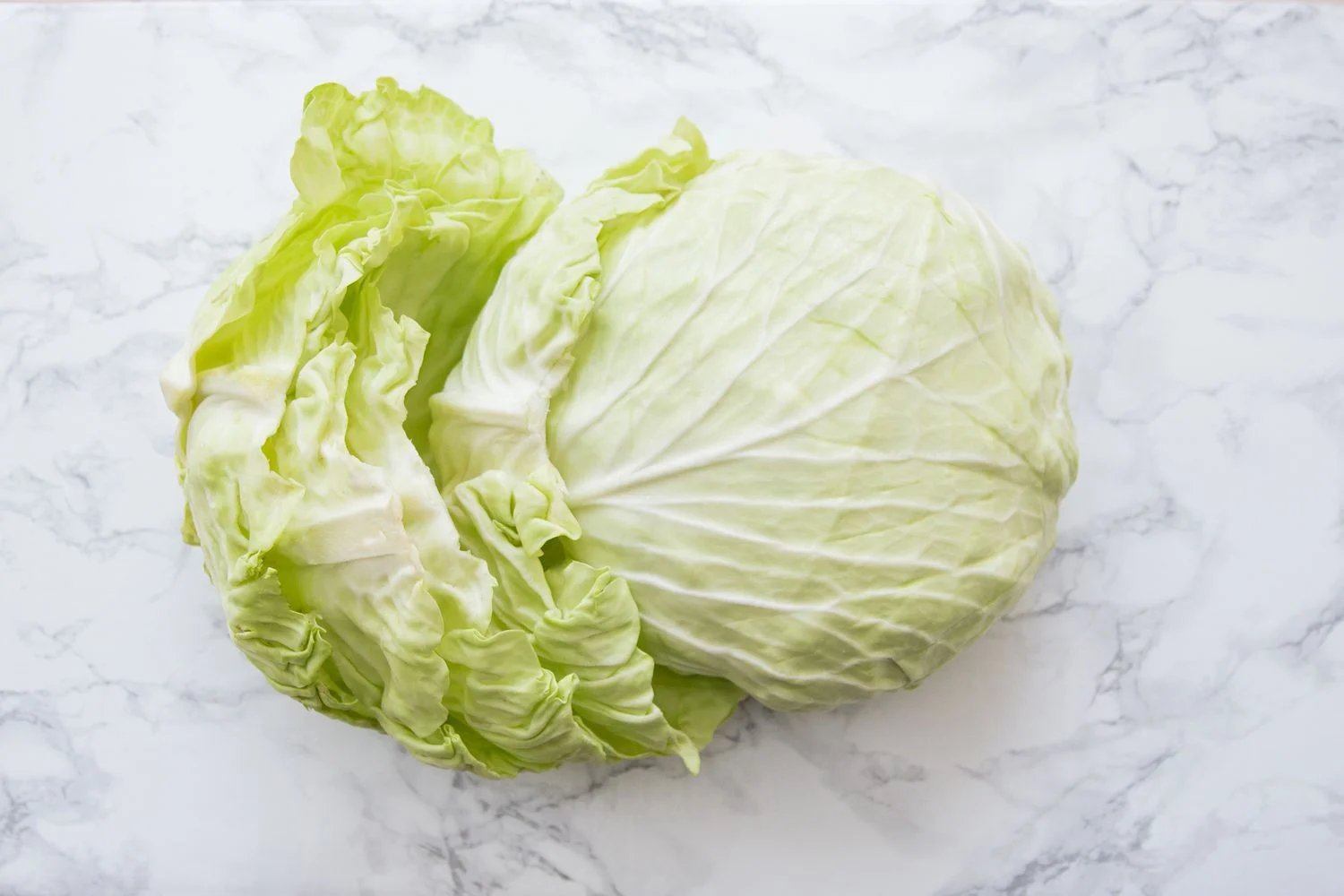 Cabbage head with leaves removed on a white marble table