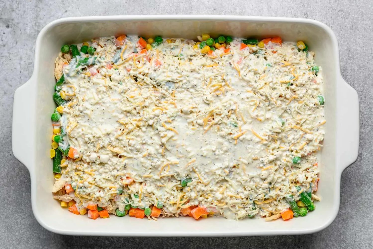 Mixture of biscuit mix, seasoning packet, milk, Italian seasoning, and cheese on top of frozen vegetables
