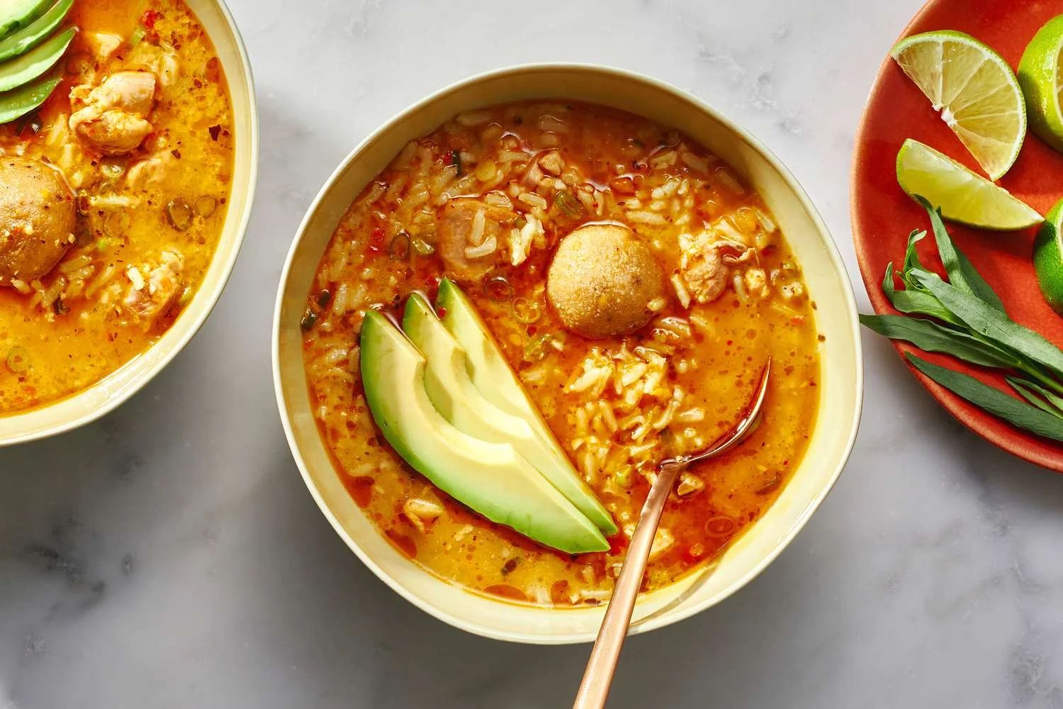 asopao de pollo in bowls with garnishes of lime and avocado slices