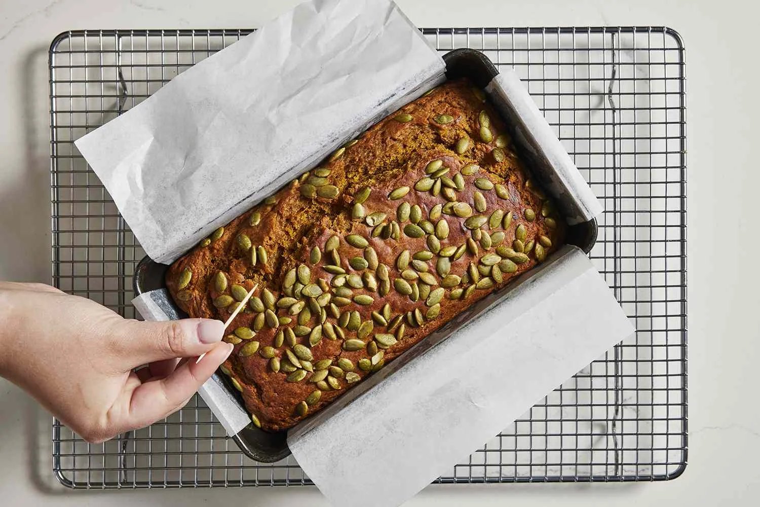 pumpkin banana bread on cooling rack, testing with toothpick