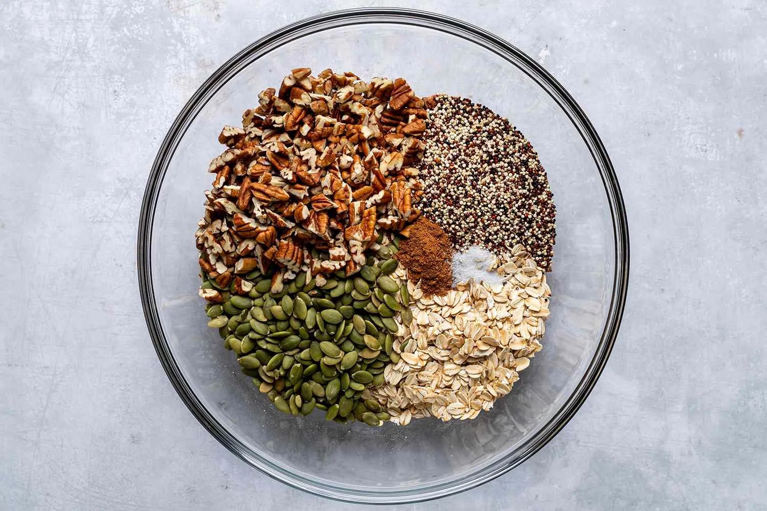 oats, pumpkin seeds, pecans, quinoa, and spices in a bowl