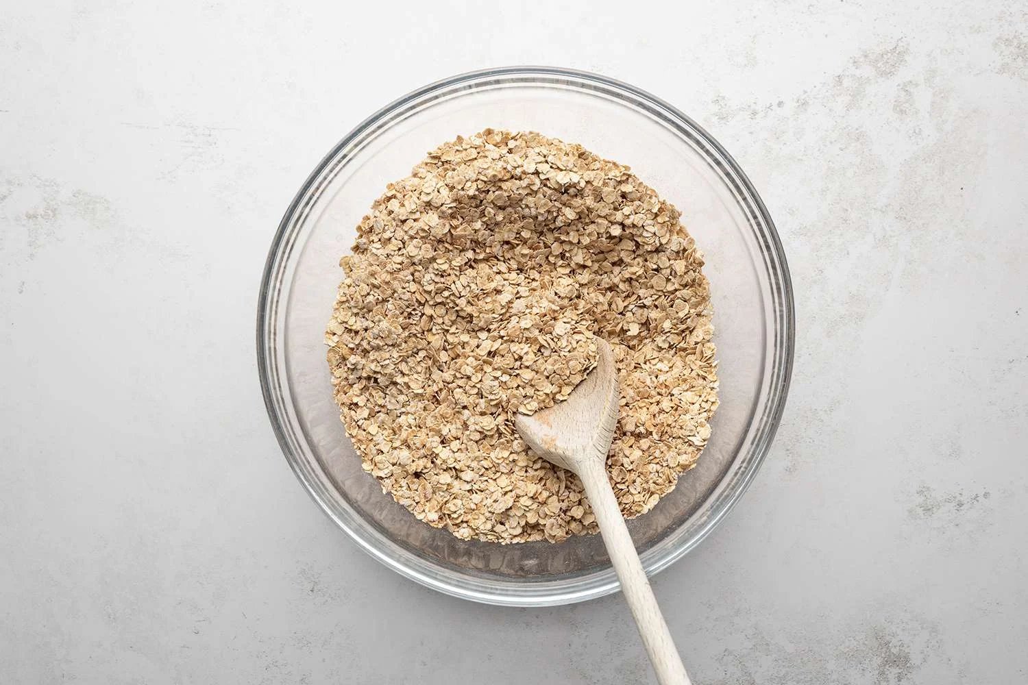 Rolled oats, baking powder, cinnamon, and salt in a bowl with a wooden spoon