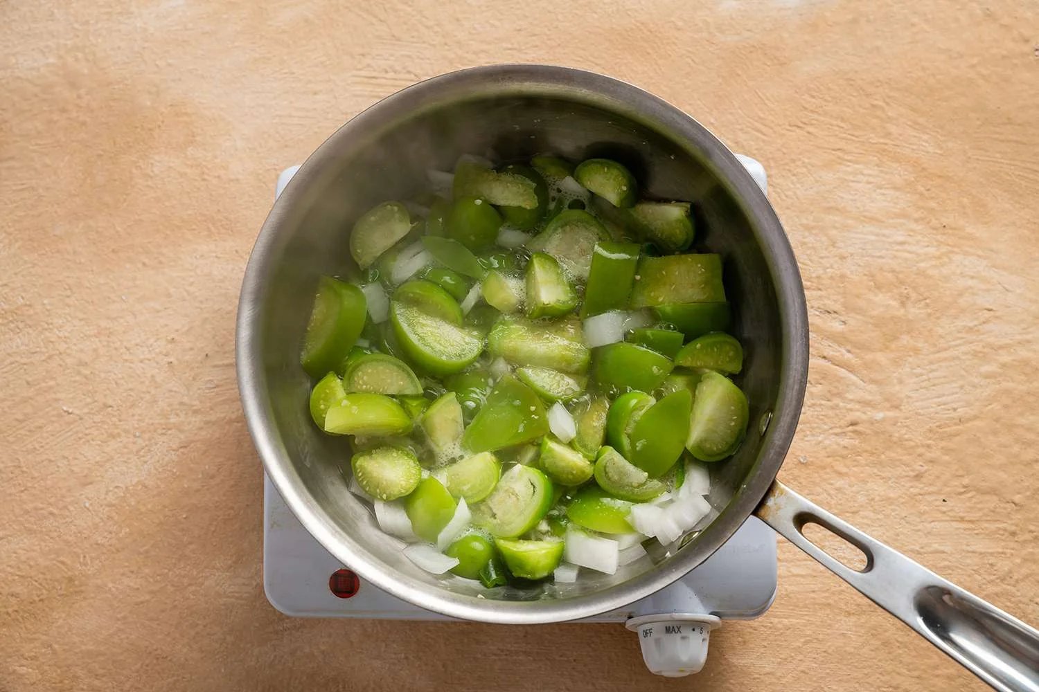 Tomatillos, onions, garlic, jalapeño, and water in a pot on a burner
