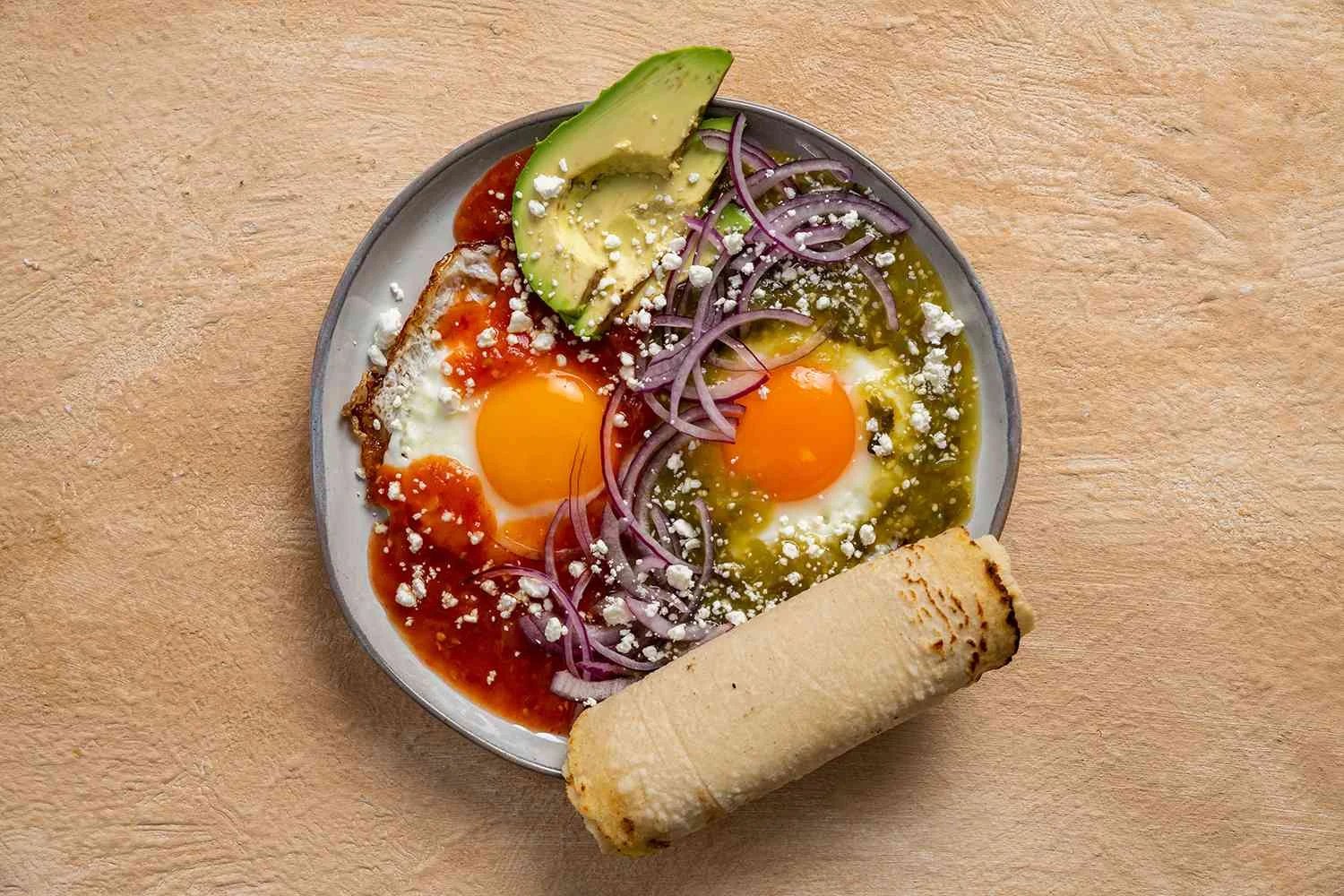 Huevos Divorciados garnished with onion, avocado, cotija cheese, and tortillas
